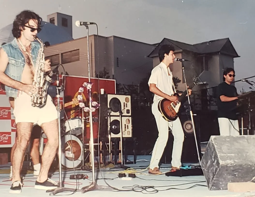 Facção Noturna tocando em palco ao ar livre nos anos 90, com guitarra e saxofone
